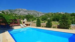 A swimming pool with lounge chairs, a stone structure, and a mountainous backdrop. - Apartment Sani by Interhome (Karlobag)