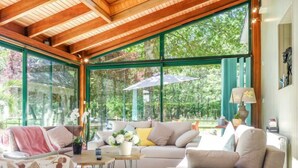 Un salon spacieux doté d’une grande fenêtre, d’un plafond en bois et d’un coin salon confortable avec un canapé et des fauteuils.