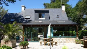 Une maison à deux étages, dotée d’un toit en pente, de grandes fenêtres et d’une terrasse aménagée avec du mobilier d’extérieur.