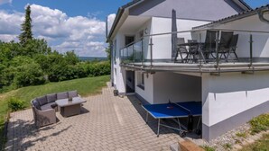 Una casa de dos pisos con balcón, zona de estar exterior y mesa de ping pong.