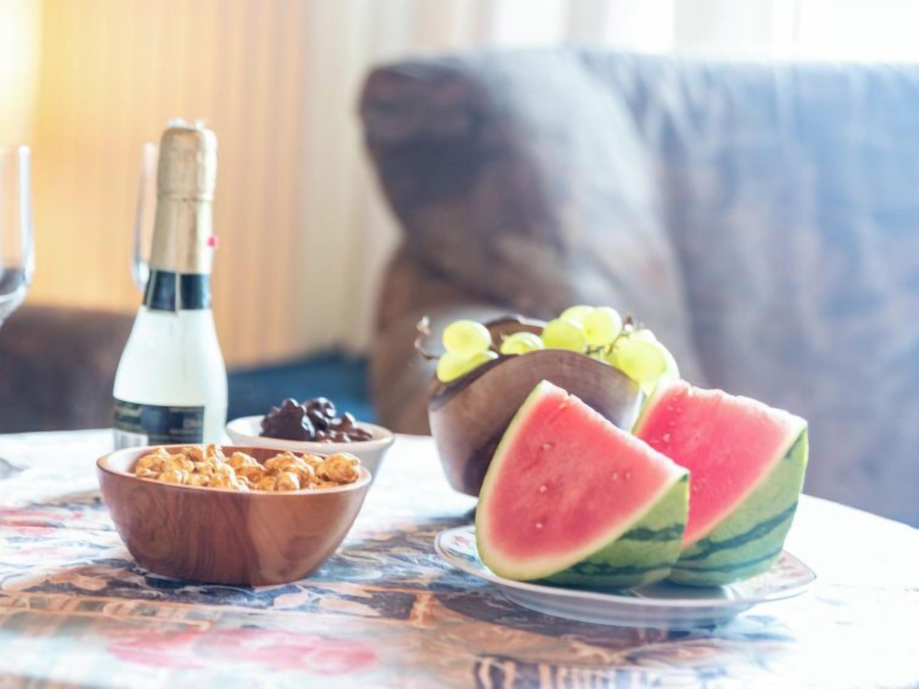 Une table avec une bouteille de champagne, un bol de granola, un bol de chocolat et une assiette de tranches de pastèque et de raisins.
