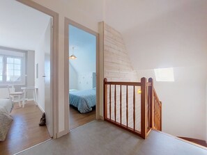 Ein Zimmer mit einem Bett, einem Schreibtisch und einem Stuhl. Eine Holztreppe mit Geländer ist vorhanden.