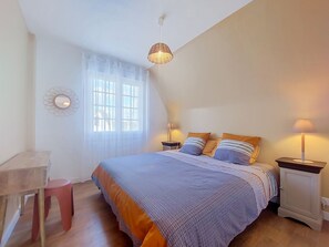 Un dormitorio con cama, lámparas de noche, ventana con cortinas, una mesita y una silla.