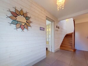 A hallway with wooden paneling, a decorative wall art piece, a door with a glass panel, and a wooden staircase.