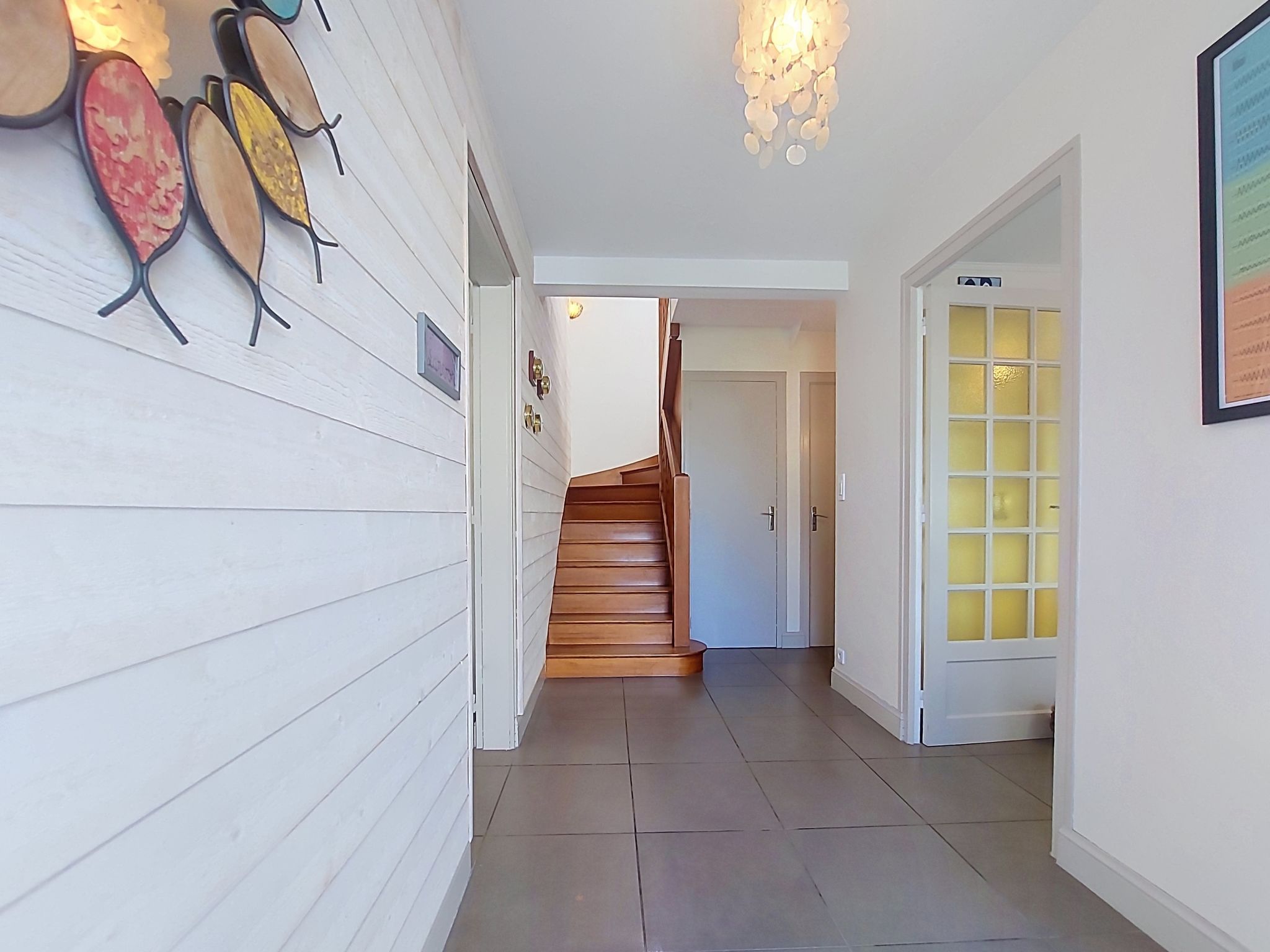 Un couloir doté d’un plancher en bois, d’un escalier et d’une porte avec un panneau en verre dépoli.