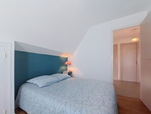 A bedroom with a bed, a nightstand, a lamp, and a door leading to another room.