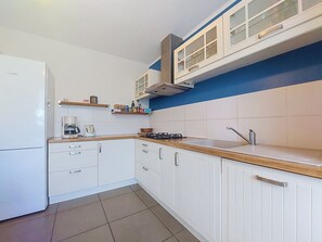 Una cocina con armarios blancos, horno empotrado, cafetera y estufa a gas.