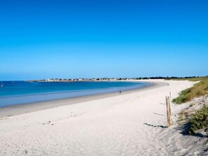 A wide sandy beach with clear blue water and a few buildings in the distance. - Sables Blancs by Interhome (Loctudy)