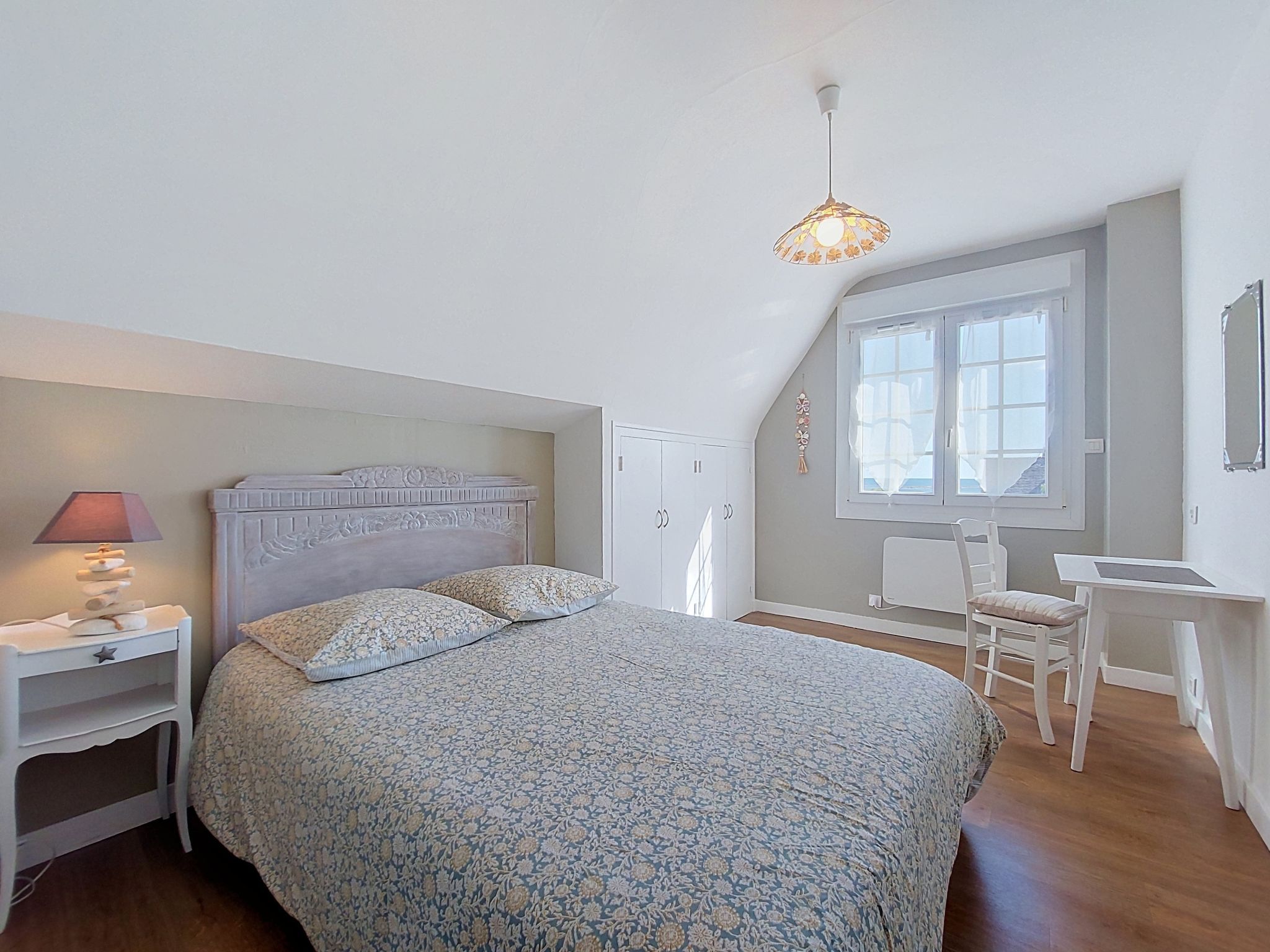 A bedroom with a bed, bedside table, lamp, and a desk with a chair.