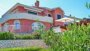 A multi-story building with a pink facade, balconies, and a stone wall in the foreground. - Jadranka by Interhome (Rab/Rab)