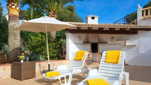 Un pati amb dues cadires còmodes blanques, un parasol beix i una petita jardiniera amb flors grogues.