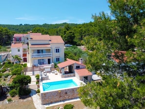 Una villa de varios pisos con piscina, rodeada de exuberante vegetación y colinas.