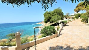 A coastal pathway leading to a beach with clear blue waters, surrounded by greenery and buildings. - Casa Taty by Interhome (El Campello/Villajoyosa)