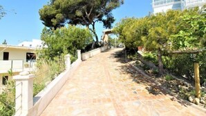 A paved pathway leading to a building with a large tree in the center. - Casa Taty by Interhome (El Campello/Villajoyosa)
