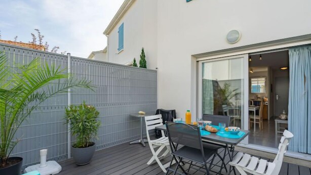 Un patio al aire libre con mesa y sillas, plantas en macetas y vistas hacia el interior de la casa.
