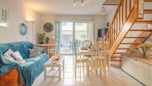 Una sala de estar con un sofá azul, sillas de madera, una mesa de comedor y una escalera.
