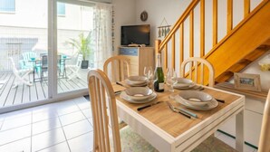 Un comedor con una mesa de madera dispuesta para cuatro personas, un televisor y una escalera.
