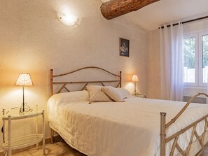 Een slaapkamer met een bed, twee nachtkastjes met lampen, een houten hoofdeinde, een schilderij aan de muur en een raam met gordijnen.