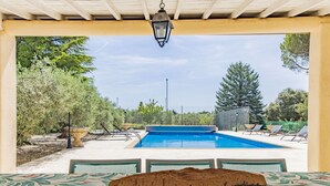 Zona de piscina con vistas a la piscina, rodeada de árboles y una zona de estar cubierta con mesa y sillas.