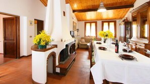 A dining area with a long table set for a meal, a fireplace, and a sofa in the background.