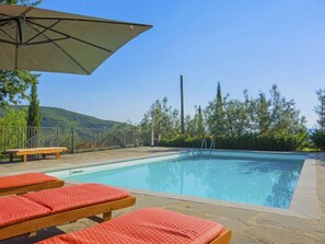 A swimming pool with lounge chairs and an umbrella, surrounded by a fence and trees.