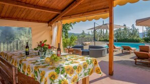 An outdoor covered patio with a pool, wooden furniture, and a table set with a sunflower tablecloth.