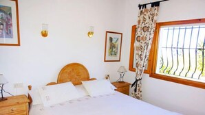 Un letto rifatto con cura, una testiera in legno, un comodino con una lampada e una finestra con tende a motivi decorativi.