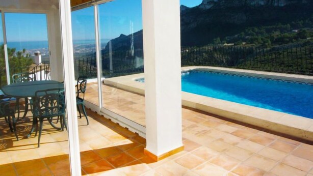Un balcone con piscina, un tavolo e sedie, affacciato su un paesaggio montano.