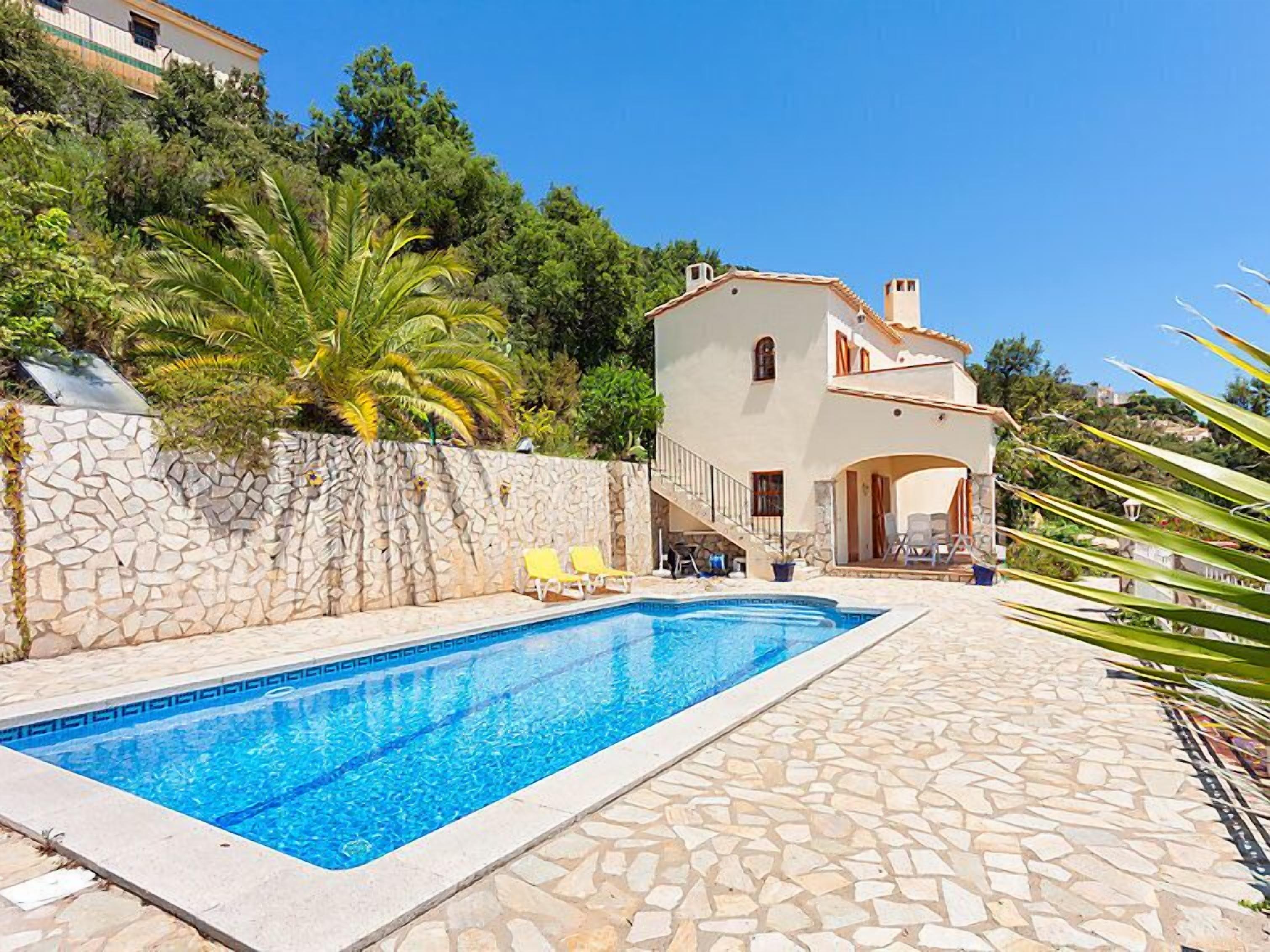A poolside area with a stone wall, a pool, and a building with a tiled roof.