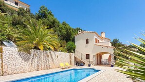 A poolside area with a stone wall, a pool, and a building with a tiled roof. - Cabanyes by Interhome (Calonge)
