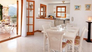 A bright kitchen with white cabinets and a dining area with wicker chairs and a white table. - Cabanyes by Interhome (Calonge)