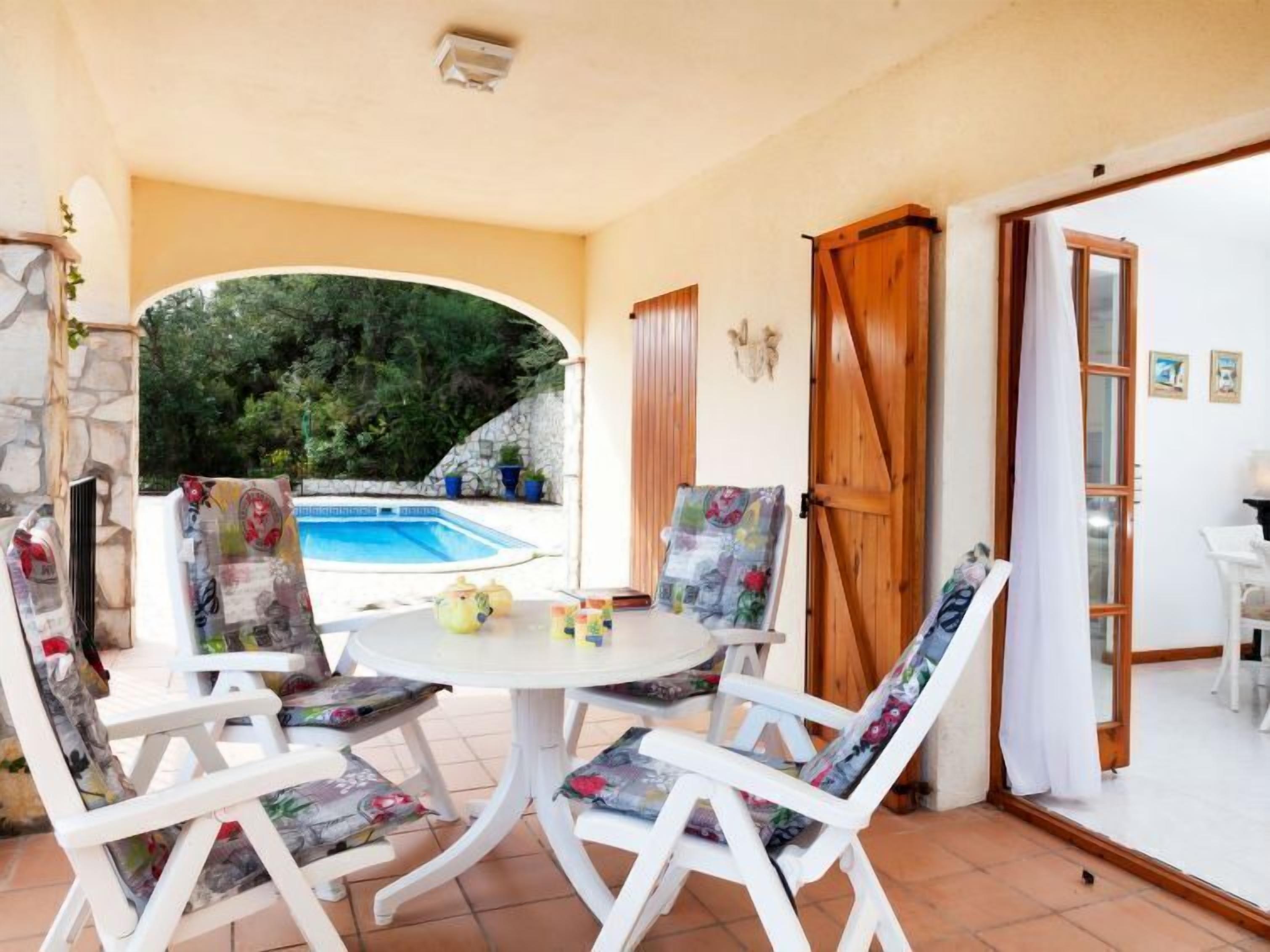 A patio with a round table and four chairs, a pool in the background, and a wooden door.