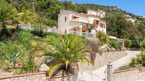 A hillside villa with a stone retaining wall, a white gate, and lush greenery. - Cabanyes by Interhome (Calonge)