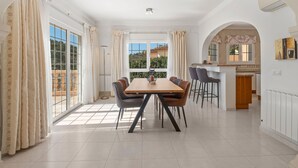 A spacious dining area with a large table and chairs, a kitchen area with a bar, and large windows with curtains. - La Perla by Interhome (Moraira)