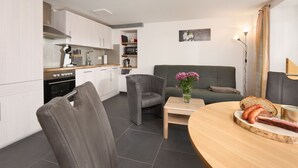A modern kitchen with white cabinets, a built-in oven, and a dining area with a round wooden table and two chairs. - Fürderer by Interhome (Eisenbach)