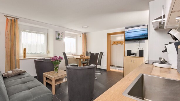 A modern living room with a grey sofa, a small table with a vase of flowers, and a dining area with chairs. - Fürderer by Interhome (Eisenbach)