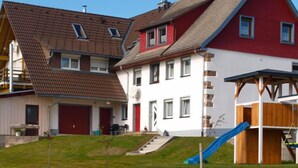 A residential area with houses featuring red and white exteriors, a visible garage, and a small playground with a slide. - Fürderer by Interhome (Eisenbach)