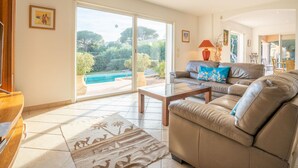 A spacious living room with a large sliding glass door leading to a pool area, a leather sofa, and a coffee table. - La Petite Afrique by Interhome (Les Issambres)