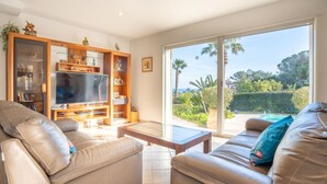 A modern living room with leather sofas, a flat-screen TV, wooden shelving, and a large sliding glass door leading to a garden. - La Petite Afrique by Interhome (Les Issambres)