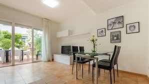 Un espace repas moderne avec une table et des chaises en verre, un téléviseur à écran plat et un meuble blanc.