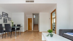 Un salon moderne comprenant un coin repas, un escalier et une cuisine visible à travers une porte ouverte.