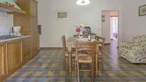 A dining area with a wooden table and chairs, a coffee machine, and a hanging light fixture.