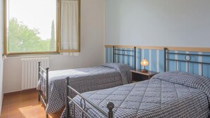 A room with two beds, a window with curtains, a radiator, and a wall-mounted light fixture.