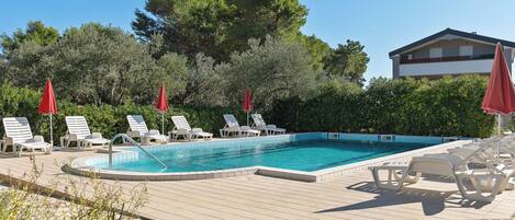 Une piscine entourée de chaises longues et de parasols rouges, avec des arbres tout autour et un bâtiment en arrière-plan.