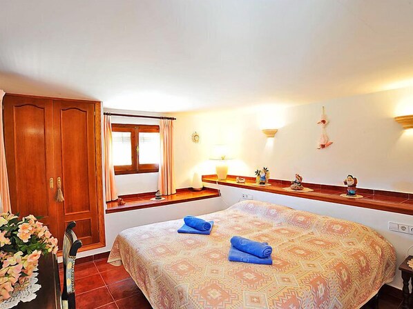 A bedroom with a large bed, a wooden wardrobe, a window with curtains, a bedside table with a lamp, and wall-mounted decorations. - Vacation home Lucie by Interhome (Jávea)