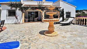 A stone patio with a decorative fountain, outdoor seating, and a building with a white facade and terracotta roof tiles. - Vacation home Lucie by Interhome (Jávea)