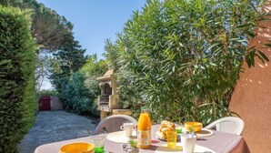 Un espace de restauration en plein air avec une table dressée pour deux personnes, entouré d’une végétation luxuriante et bordé d’un chemin en pierre.