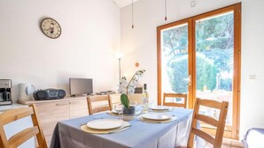 Un coin repas avec une table dressée pour quatre personnes, une machine à café, un téléviseur et une vue sur une forêt, visible à travers une porte vitrée.