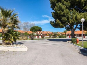 A spacious parking lot with a clear sky, surrounded by buildings with red-tiled roofs and palm trees.
