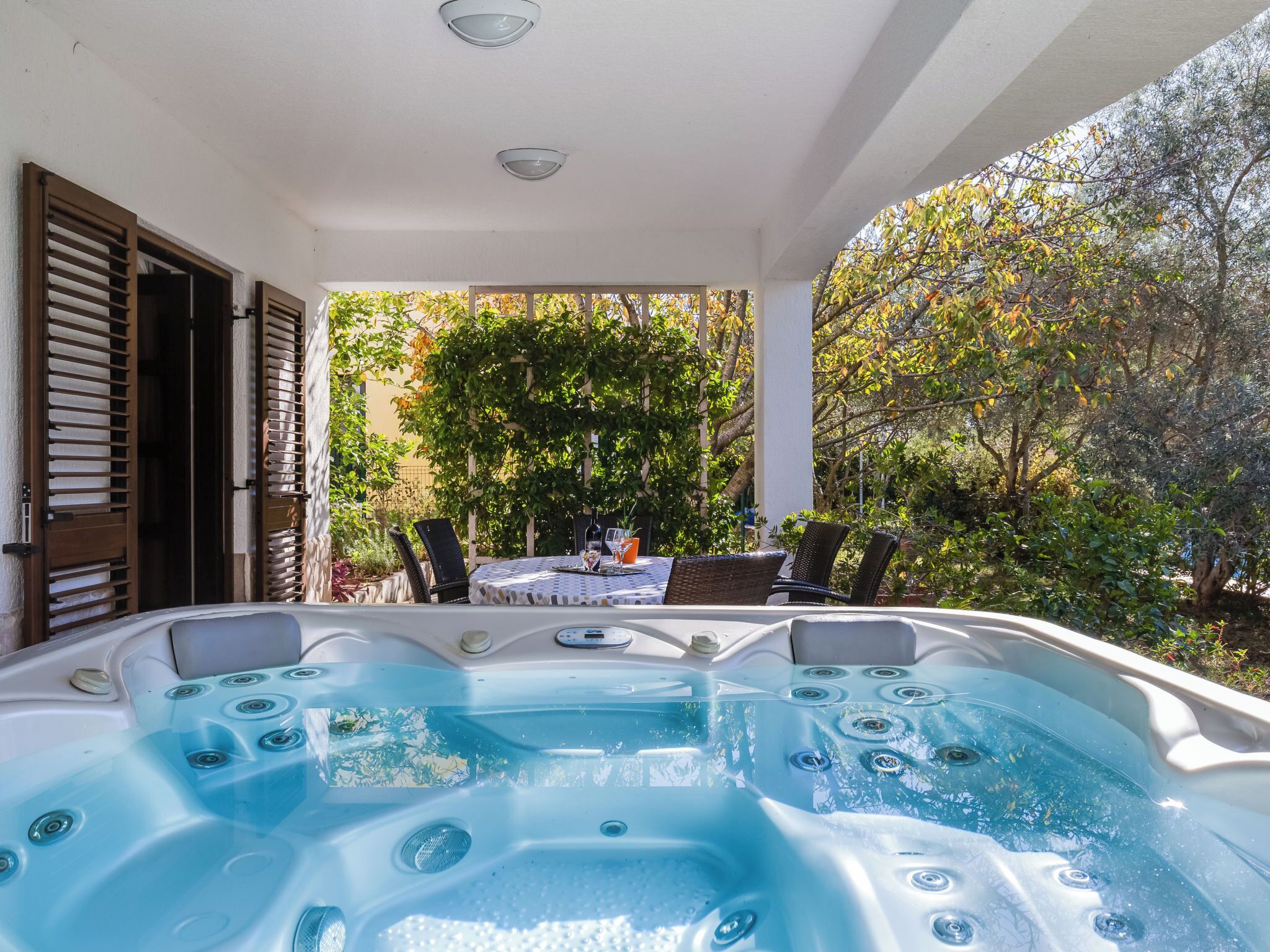 Un área de hidromasaje con una mesa y sillas, rodeada de árboles y una pérgola.